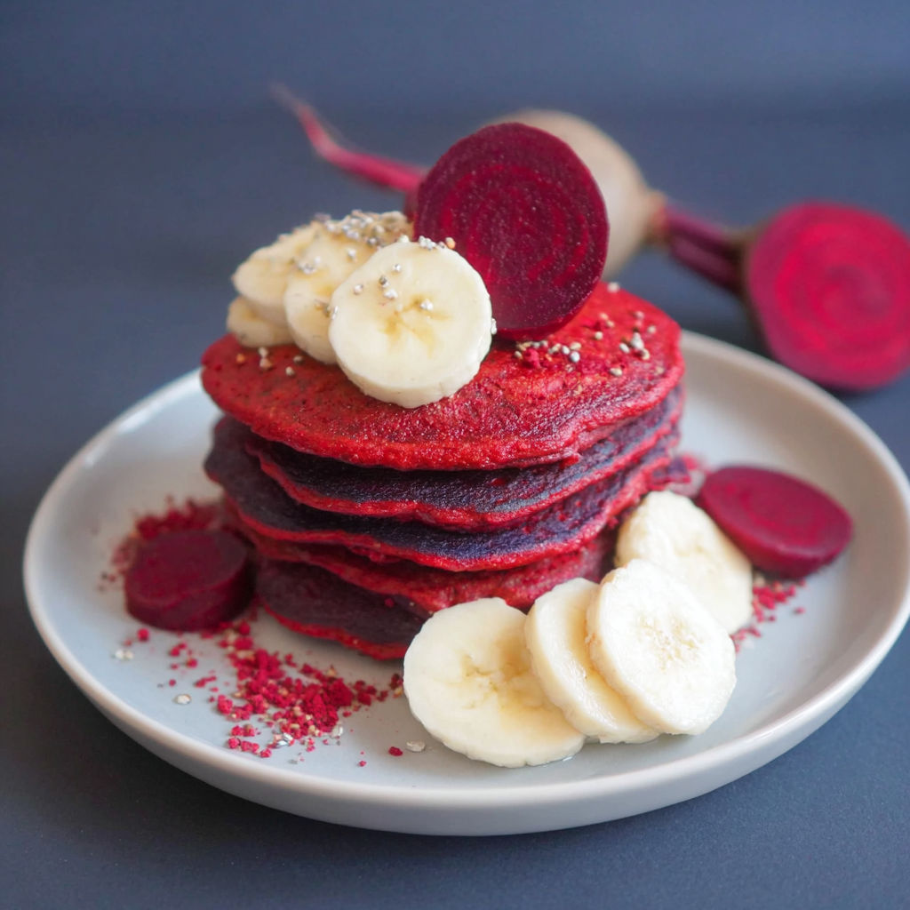 A stack of red velvet pancakes with bananas on top.