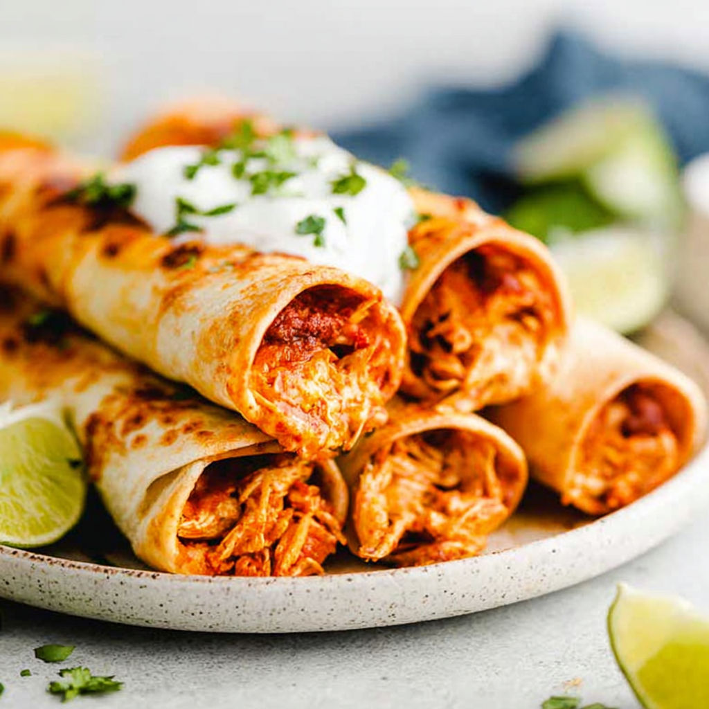 Baked cream cheese chicken taquitos with limes on the side.