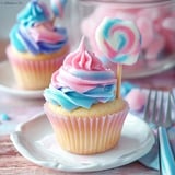 A cupcake with a pink and blue frosting and a lollypop stick in it.