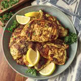 A plate of marinated chicken with lemon wedges on top.