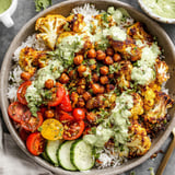 A bowl of food with rice, tomatoes, cucumbers, and cauliflower.