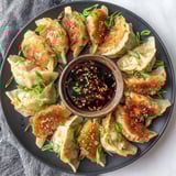 A plate of chicken potstickers with a bowl of sauce.