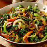 A pan of sautéed vegetables, including broccoli and carrots, on a wooden cutting board.