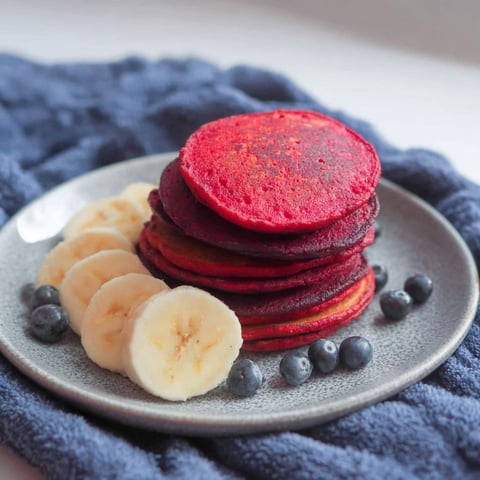 A stack of red pancakes with blueberries on top.